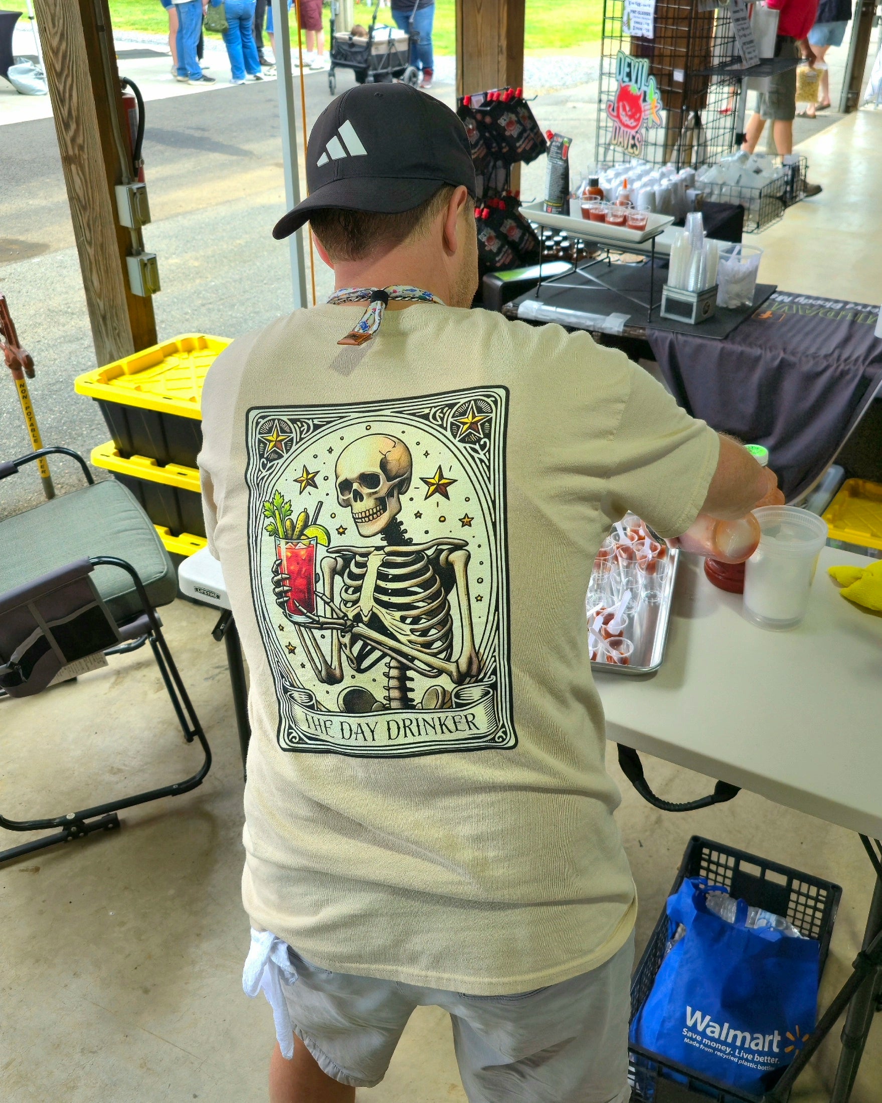 Person wearing a day drinker Tarot card t-shirt with a holding a Bloody Mary cocktail design at an outdoor event.