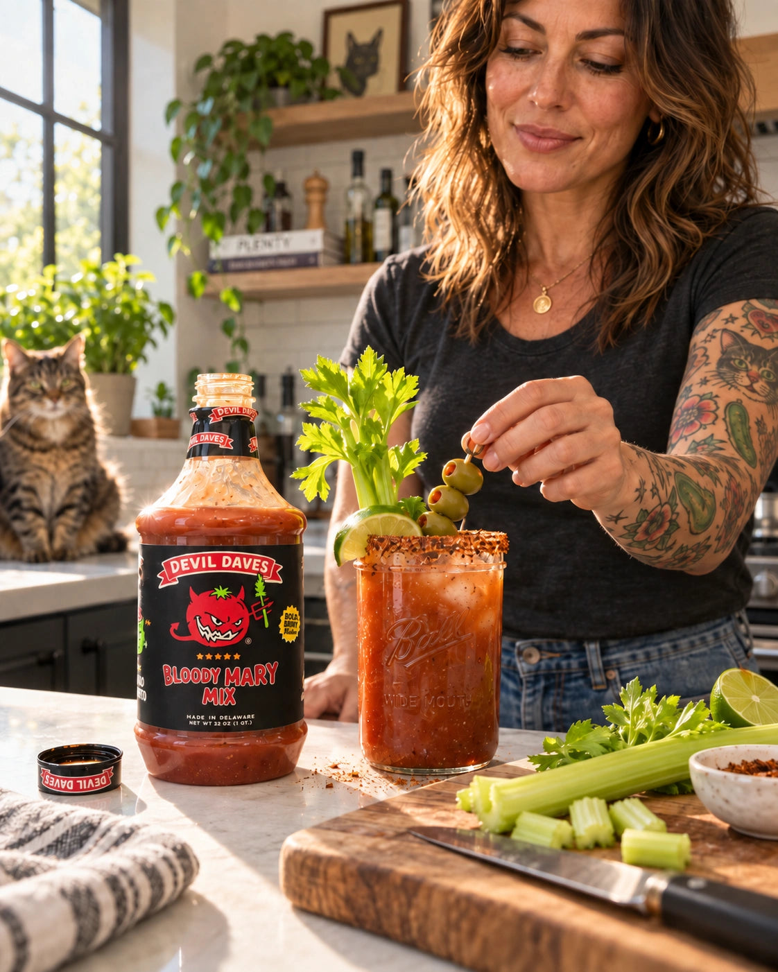 A middle-aged woman making a bloody mary cocktail with devil Daves 32 oz mix in a kitchen. The woman has arm tattoos of cats and pickles with a cat in the background. 