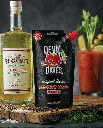 Texacraft pickle brine bottle and Devil Daves Bloody Mary mixer on a wooden surface with a cocktail in the background.