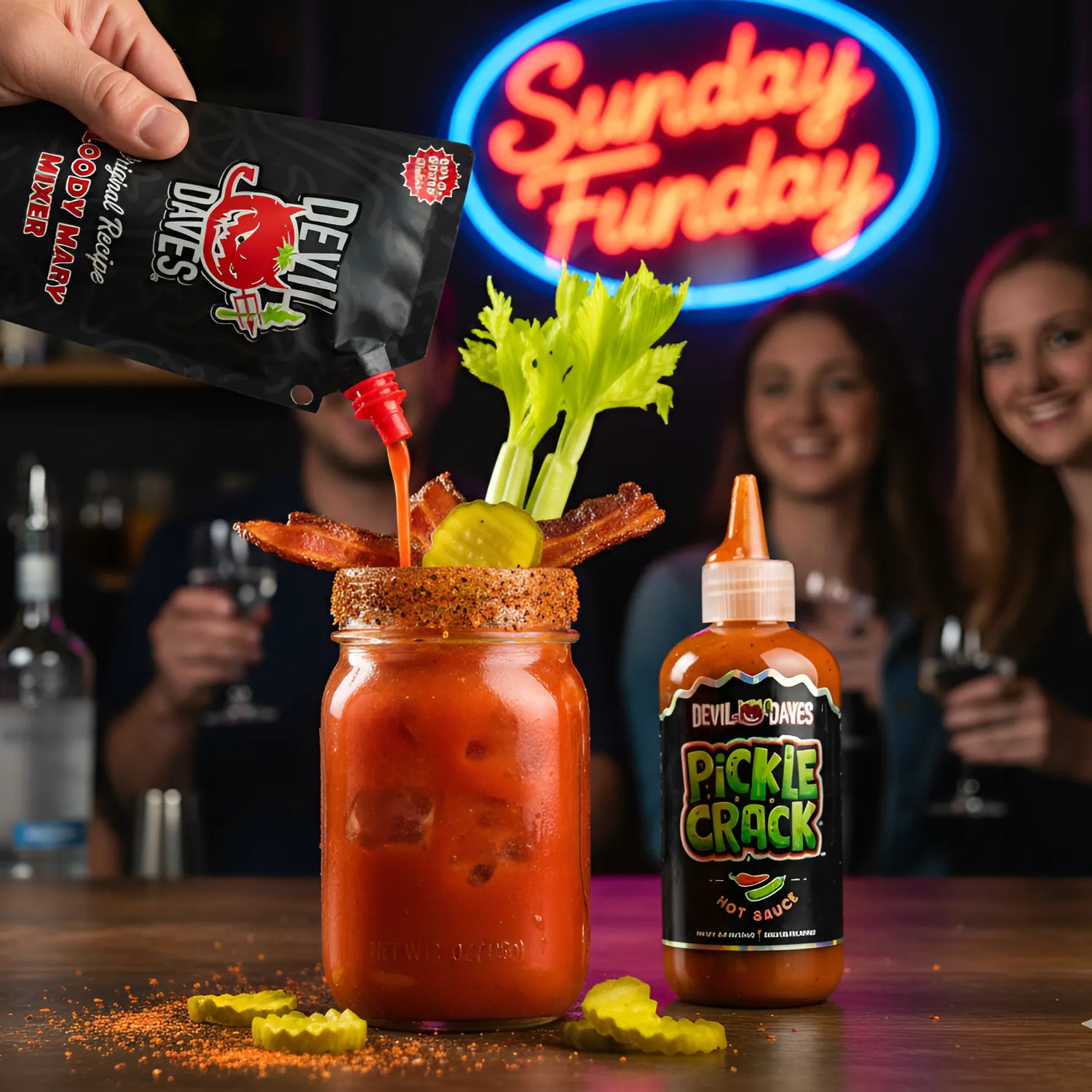 a bloody mary being poured from Devil Daves travel pouch into a mason jar with bacon and celery garnish. A bottle of pickle hot sauce sits next to the glass and the scene shows surrounded by people and 'Sunday Funday' neon sign