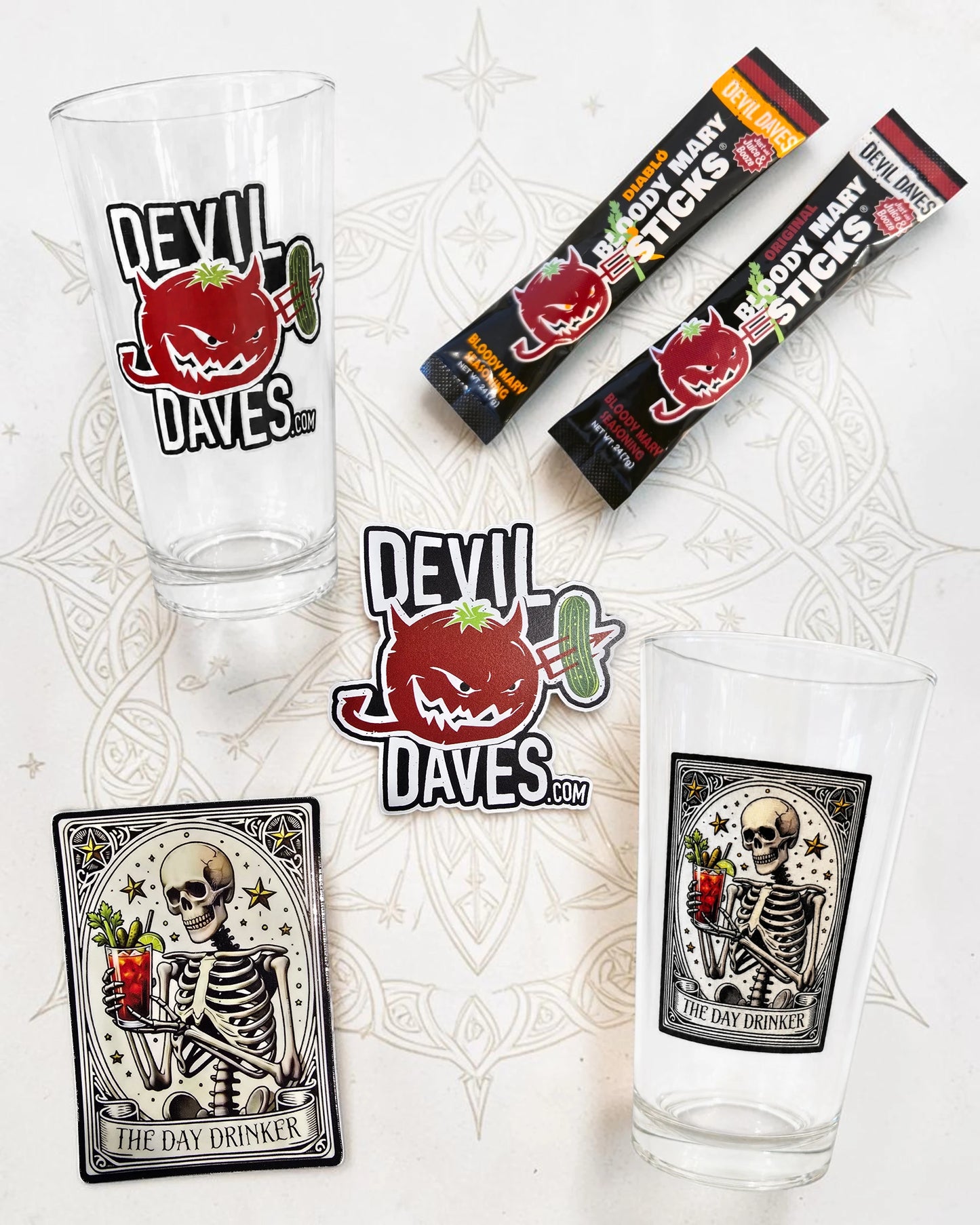 Two glass mugs with 'Devil Daves' branding, a pack of 'Devil Daves' sticks, and a skeleton-themed coaster on a decorative white background.